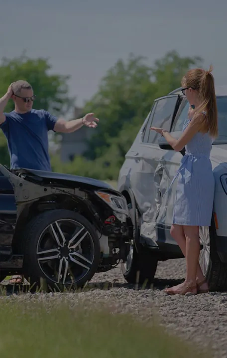 A man and woman stand next to two damaged cars after a collision, appearing to discuss the accident on a sunny day.