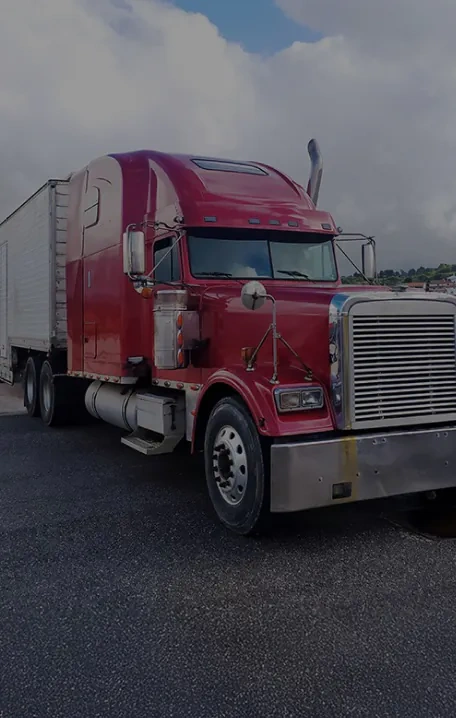 A red semi-truck with a sleeper cab is parked on an asphalt surface under a cloudy sky, attached to a white trailer.