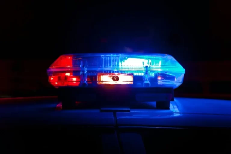 Close-up of a California police car roof with red and blue emergency lights illuminated against a dark background.