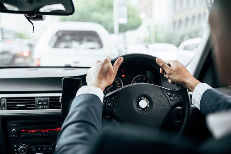 A person in a suit drives a car, holding the steering wheel with both hands while waiting in traffic behind other vehicles—highlighting how everyday moments can be impacted by auto accident statistics from 2020.