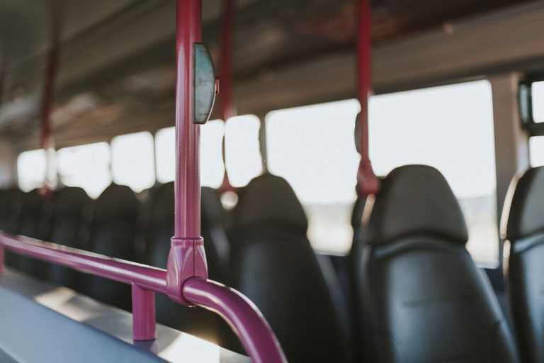 Rows of empty black seats and pink poles inside a California bus, with sunlight streaming through the windows.