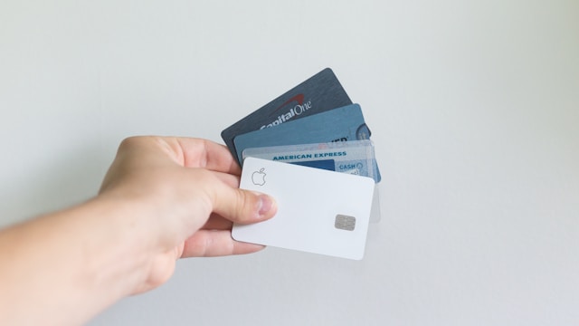 A hand displays a fanned-out group of credit cards, including an Apple Card and an American Express, against a plain light background—perfect for illustrating California law topics like statute of limitations or premises liability claims.
