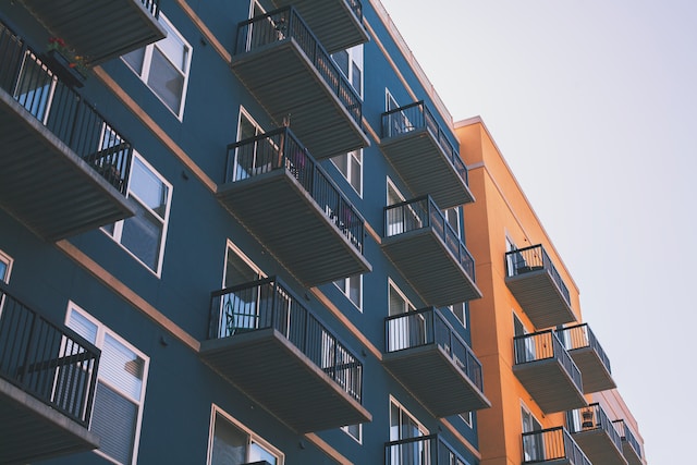 Exterior view of a modern rented apartment building with multiple balconies, featuring blue and orange painted walls against a clear sky.