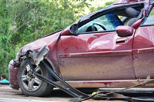 A heavily damaged red car with a shattered windshield and crushed side panels, loaded onto a flatbed tow truck in an outdoor setting, suggests an incident where compensation might be pursued, similar to slip and fall cases in a rented apartment.