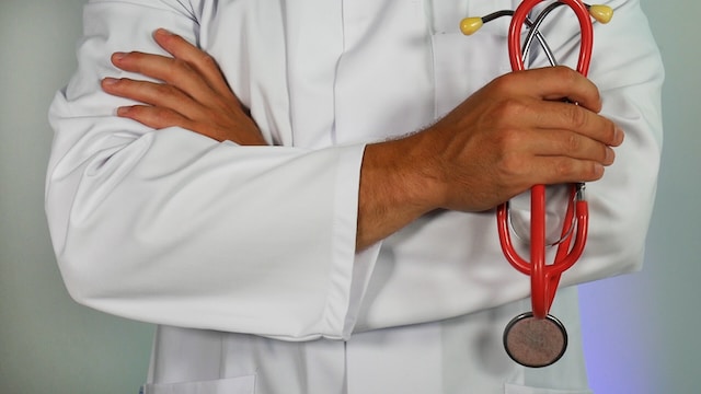 Person in a white lab coat stands with arms crossed, holding a red stethoscope in one hand, ready to discuss California's ignition interlock device requirements.