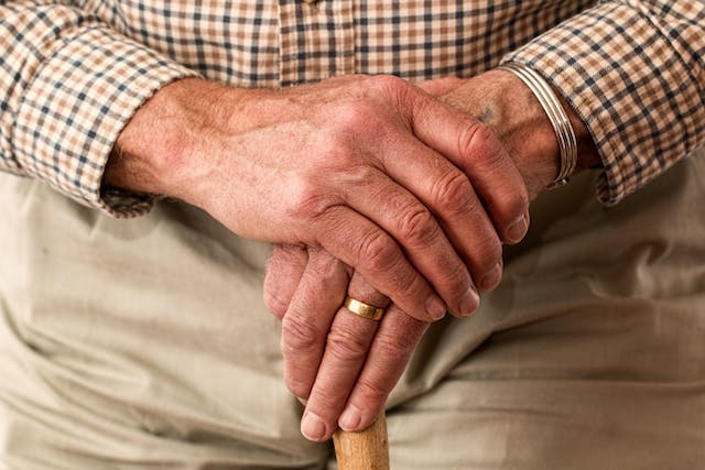 Close-up of an elderly person's hands resting on a cane, wearing a gold ring and a checkered shirt, reminiscent of someone reflecting on life changes after facing DUI penalties.