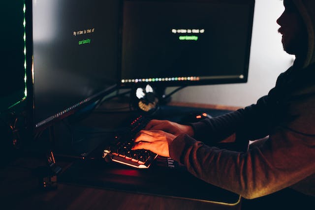A person in a hoodie types on a keyboard at a desk with two monitors displaying lines of green text, researching premises liability claims and the statute of limitations California enforces.