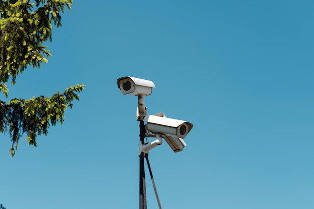 Two security cameras mounted on a pole against a clear blue sky, with part of a tree visible on the left side—mirroring the vigilance required to avoid penalties or jail time for a Third DUI in California.