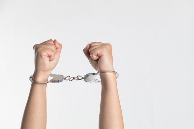 Two hands raised in the air, secured together with metal handcuffs against a plain white background—much like the common symptoms felt after a car crash, there’s a sense of shock and restraint in this stark image.