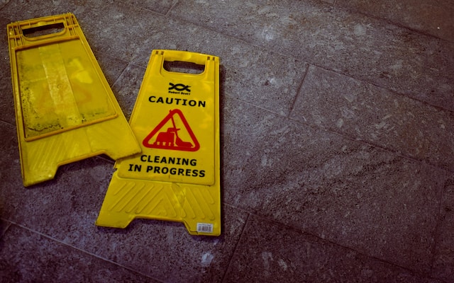 Two yellow "Caution: Cleaning in Progress" signs lie flat on a dark tiled floor, a scene reminiscent of the aftermath of a car crash, where concussion symptoms and common symptoms require careful attention to safety.