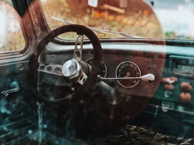 Close-up view of the steering wheel and dashboard of an old car, seen through a slightly dirty window—a haunting reminder of Halloween Drunk Driving Accidents and the importance of staying safe on the roads.