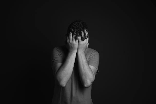 A person stands against a dark background with their head bowed and both hands covering their face, expressing the distress often felt after an accident in Sacramento.