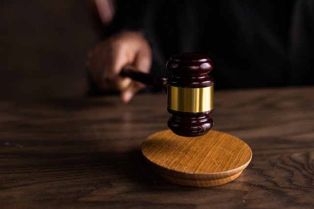A hand holds a wooden gavel above a round sound block on a wooden table, suggesting a judicial or courtroom setting where a California dispute over a breathalyzer might be decided.