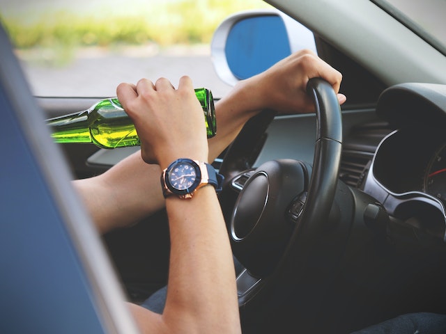 A person grips the steering wheel with one hand and a green bottle with the other—an image that highlights the risks of DUI California and the serious consequences, including a possible jury trial for DUI California.