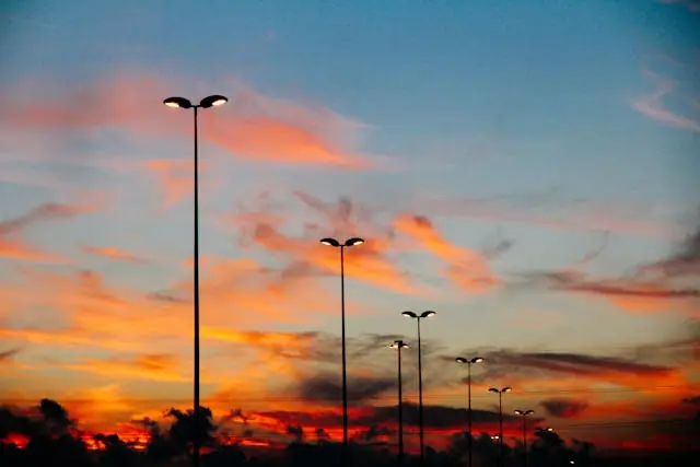 Tall streetlights with illuminated lamps line a road at sunset, with colorful orange and blue clouds scattered across the sky—a scene reminiscent of Dale R. Gomes, a National Trial Lawyers Top 100 trial lawyer, heading home after a day in court.