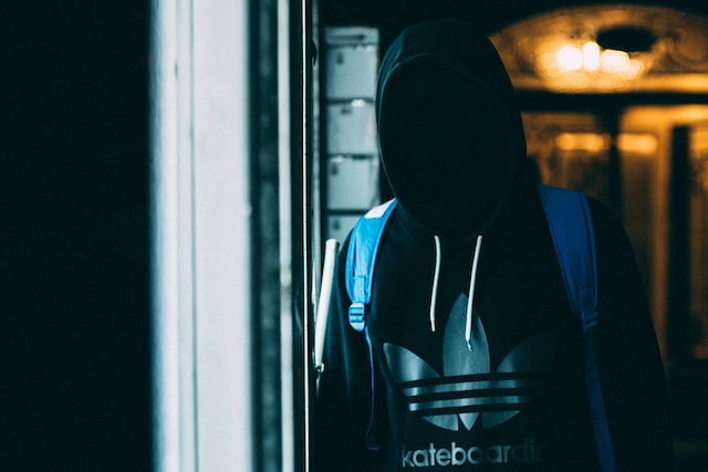 A person wearing a black hooded sweatshirt with a blue backpack stands in a dimly lit area; their face is obscured by shadow, evoking the seriousness faced by those confronting jail for third DUI offenses in California.