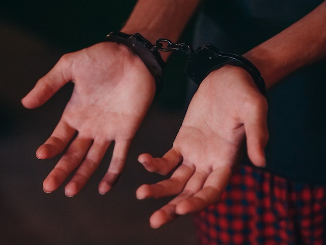 Person’s hands in handcuffs, palms facing upward, wrists restrained after a self-driving car DUI in California. The person is wearing a dark shirt and red plaid pants.