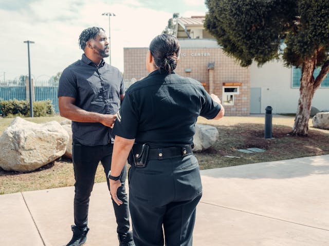 A security officer talks to a man outside near a building, with large rocks and trees in the background—perhaps discussing jail for third DUI or other California DUI penalties.