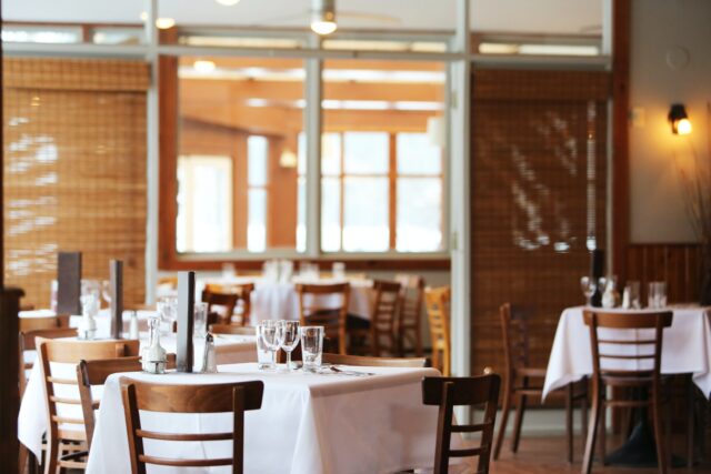 A restaurant dining area with wooden chairs, tables covered with white tablecloths, and glassware set, with large windows and natural light—an inviting space where knowing what to do after a restaurant accident is important for your safety.