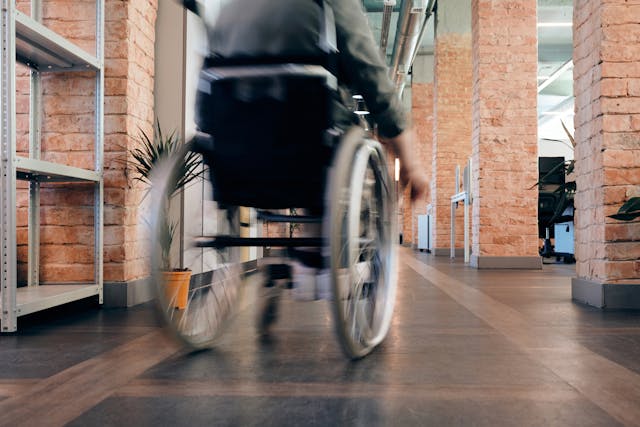 A person in a wheelchair moves through a California office space with exposed brick walls and shelves, highlighting accessibility concerns that can play a role in premises liability claims.