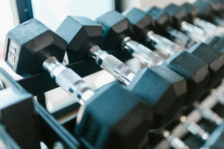 Close-up of black hexagonal dumbbells arranged on a metal rack in a gym, highlighting the impact consistent workouts can have on reducing the chances of an injury claim.