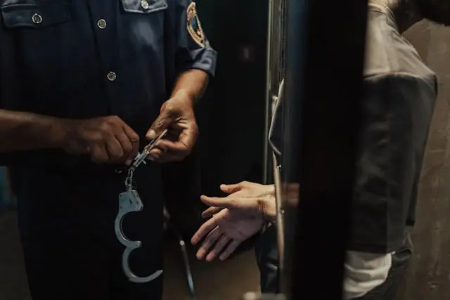 A police officer is placing handcuffs on a person’s wrists inside a dimly lit room, both figures partially visible—a scene often encountered by Esq. Dale R. Gomes, recognized by National Trial Lawyers Top 100.