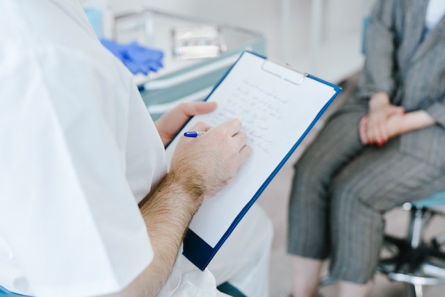 A person in a white coat writes on a clipboard while sitting across from another seated person in business attire, possibly discussing important topics such as child abuse penalties in California.