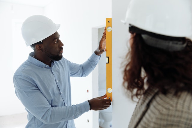 A man in a hard hat uses a spirit level against a wall while another person in a hard hat observes, ensuring there’s no dispute over precision on this California construction site.