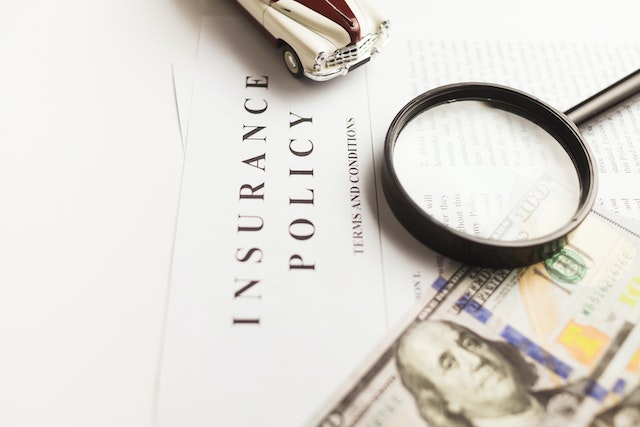 A magnifying glass, a toy car, and a hundred-dollar bill rest on an insurance policy document, hinting at DUI penalties and possible jail time after a third DUI in California.