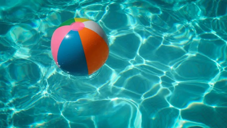 A colorful beach ball floats on the surface of a clear blue swimming pool with sunlight reflecting on the water, creating a serene scene worthy of relaxation—perfect for unwinding after a day at Dale R. Gomes, Esq., National Trial Lawyers Top 100.