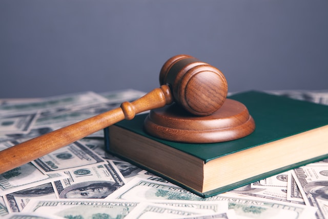 A wooden gavel rests on a green book, which is placed atop scattered US hundred dollar bills—symbolizing the financial stakes and timeline often involved in a personal injury lawsuit California.