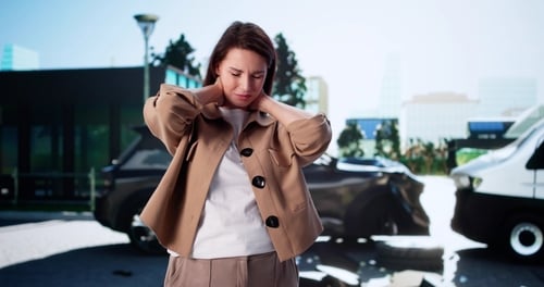 Woman holding neck beside damaged vehicles after collision on city street